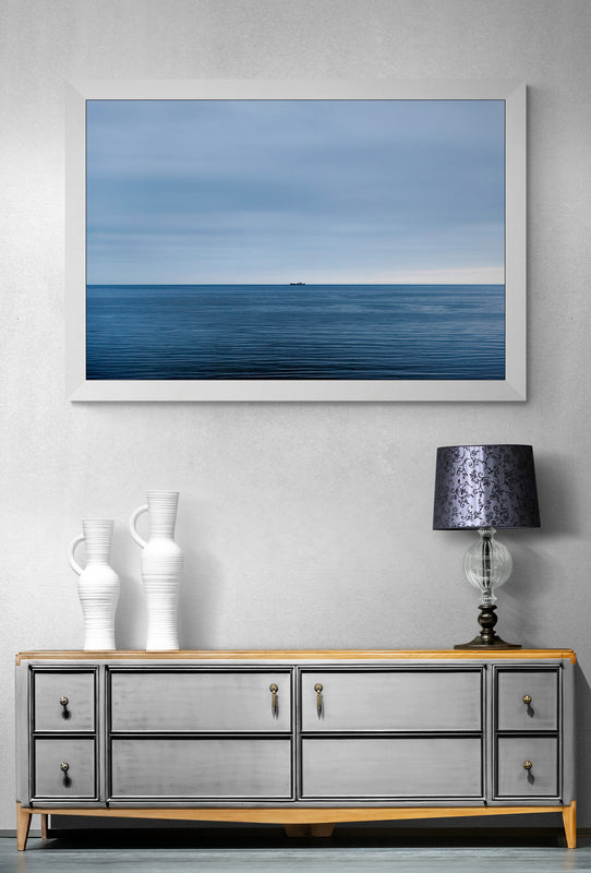 An image of a boat on the sea at the horizon line. Blue sea and blue clouds in a calm weather. 